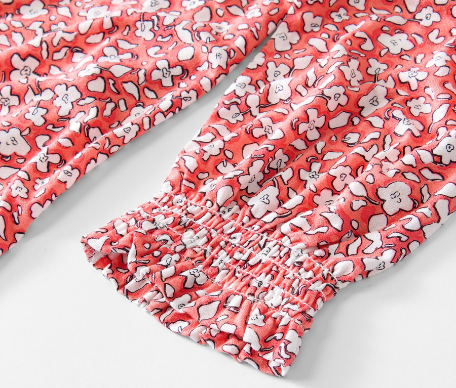 Detailansicht eines korallenfarbenen, bedruckten Blusenshirts mit langen Ärmeln.