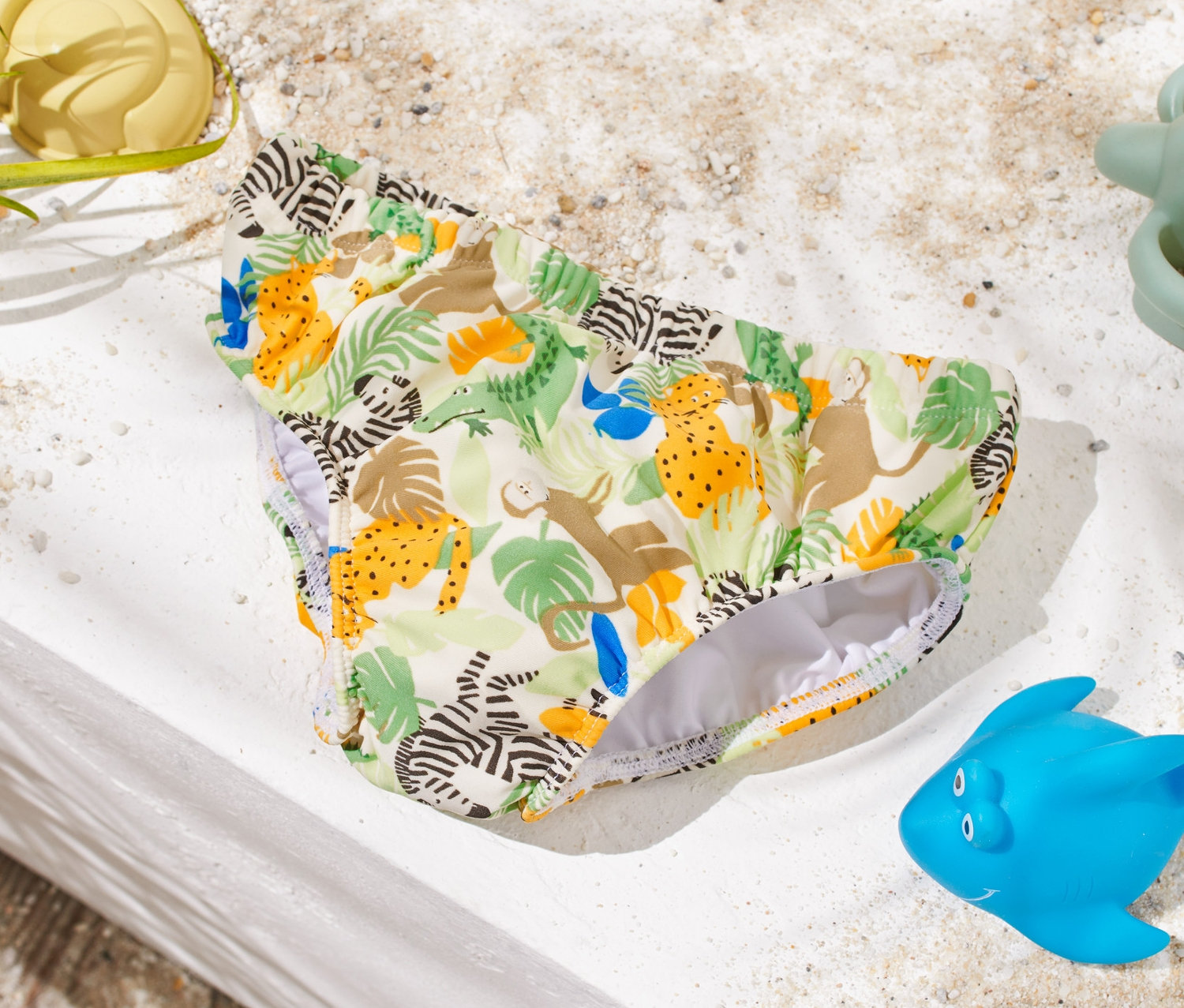 Eine Baby-Schwimmwindel mit Tiermuster liegt auf einer weißen Oberfläche neben Sandspielzeug.