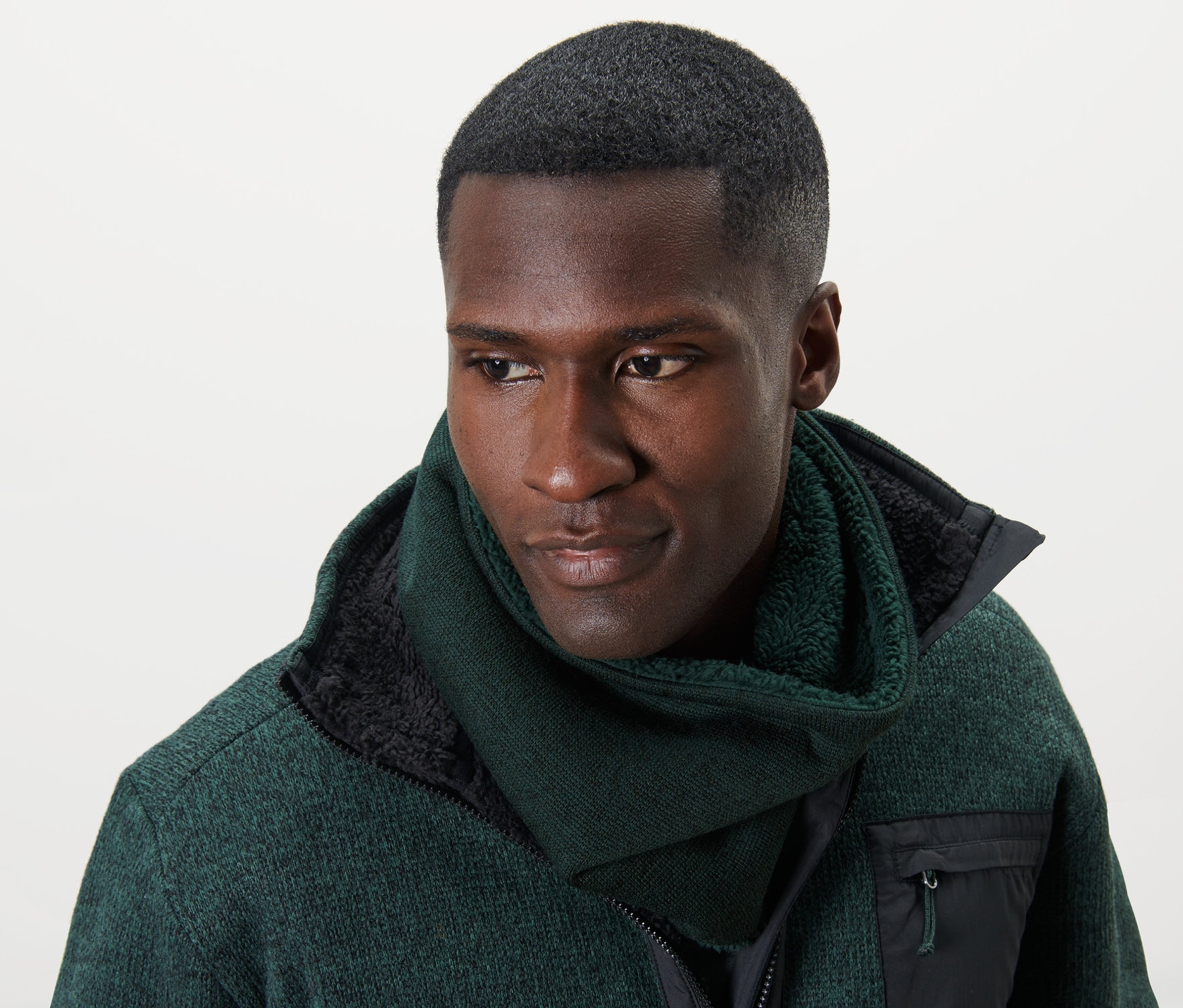 Mann trägt einen grünen Strickfleece-Schlauchschal und eine grüne Jacke.