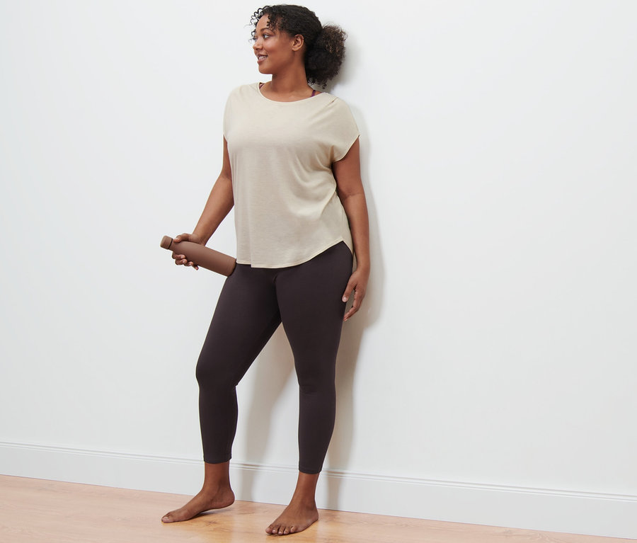 Frau hält eine braune Wasserflasche und trägt ein beiges Sportshirt und Sporttight.