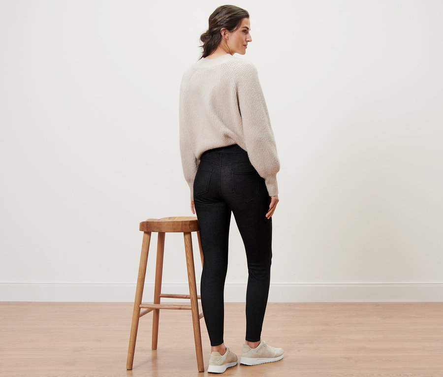 Frau steht mit dem Rücken zur Kamera, trägt gefütterte Leggings in Jeansoptik und einen Pullover.