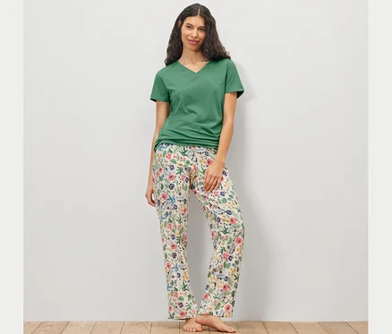 Frau trägt ein Pyjama-Set mit einer geblümten Hose und einem grünen T-Shirt.