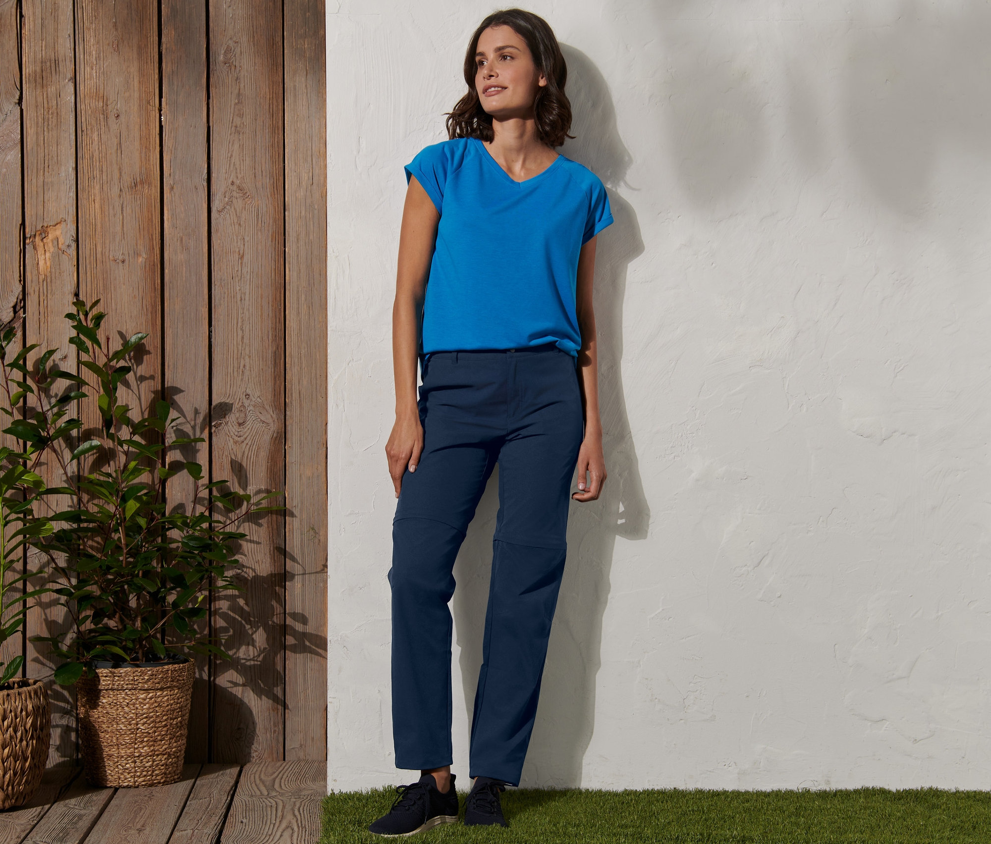 Frau steht an einer Wand und trägt eine blaue 2-in-1-Funktionshose.