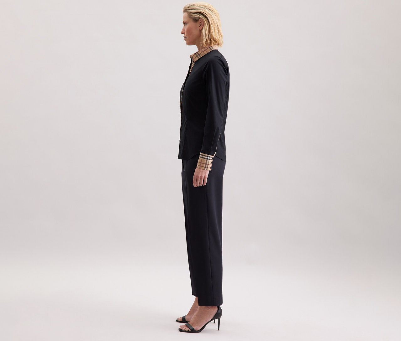 Frau im Profil trägt eine Seidensticker Popeline-Bluse mit Karodetail, dunkle Hose und Sandalen mit Absatz.