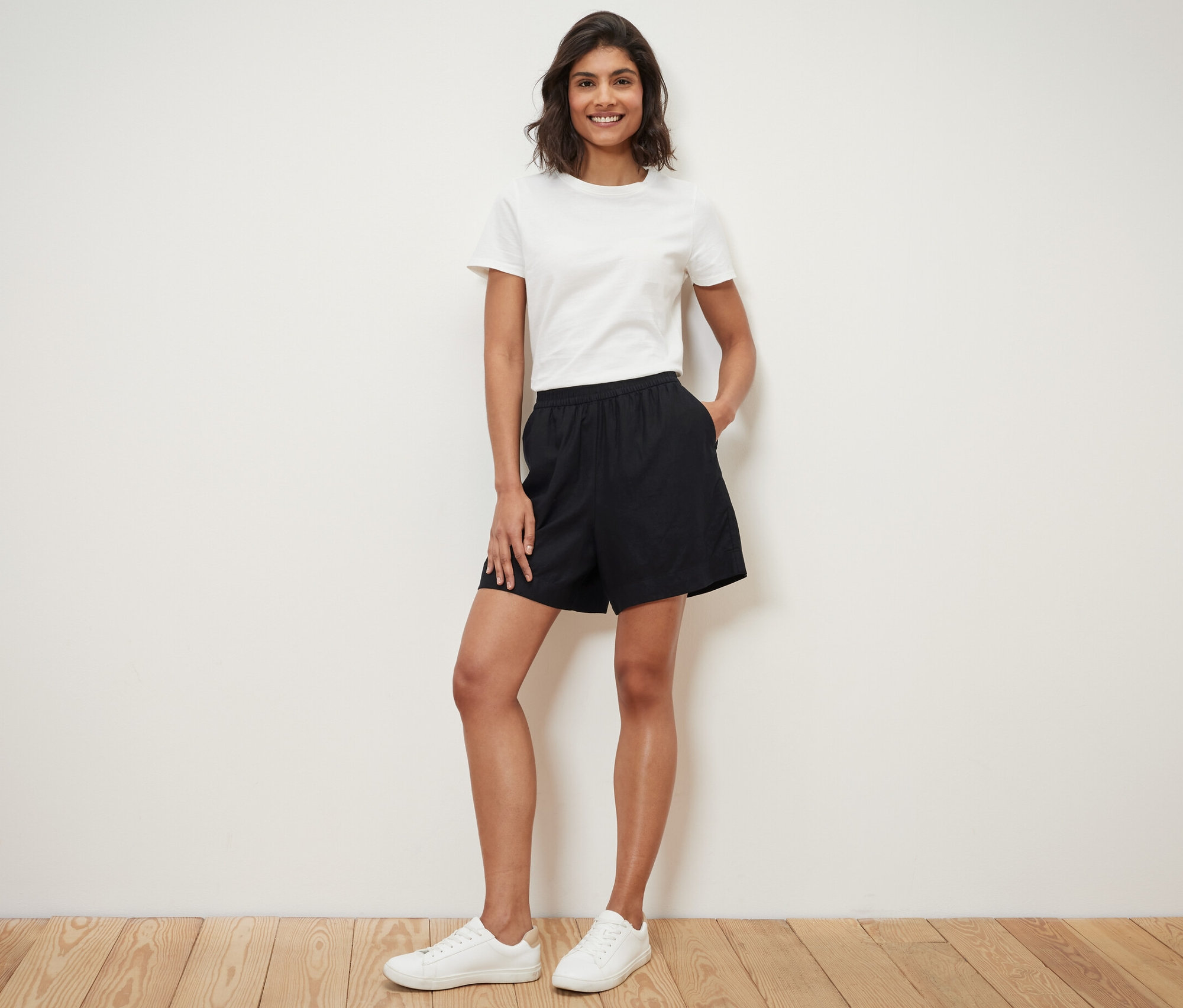 Frau steht mit Händen in den Taschen ihrer schwarzen Leinenshorts.