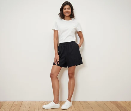 Frau steht mit Händen in den Taschen ihrer schwarzen Leinenshorts.