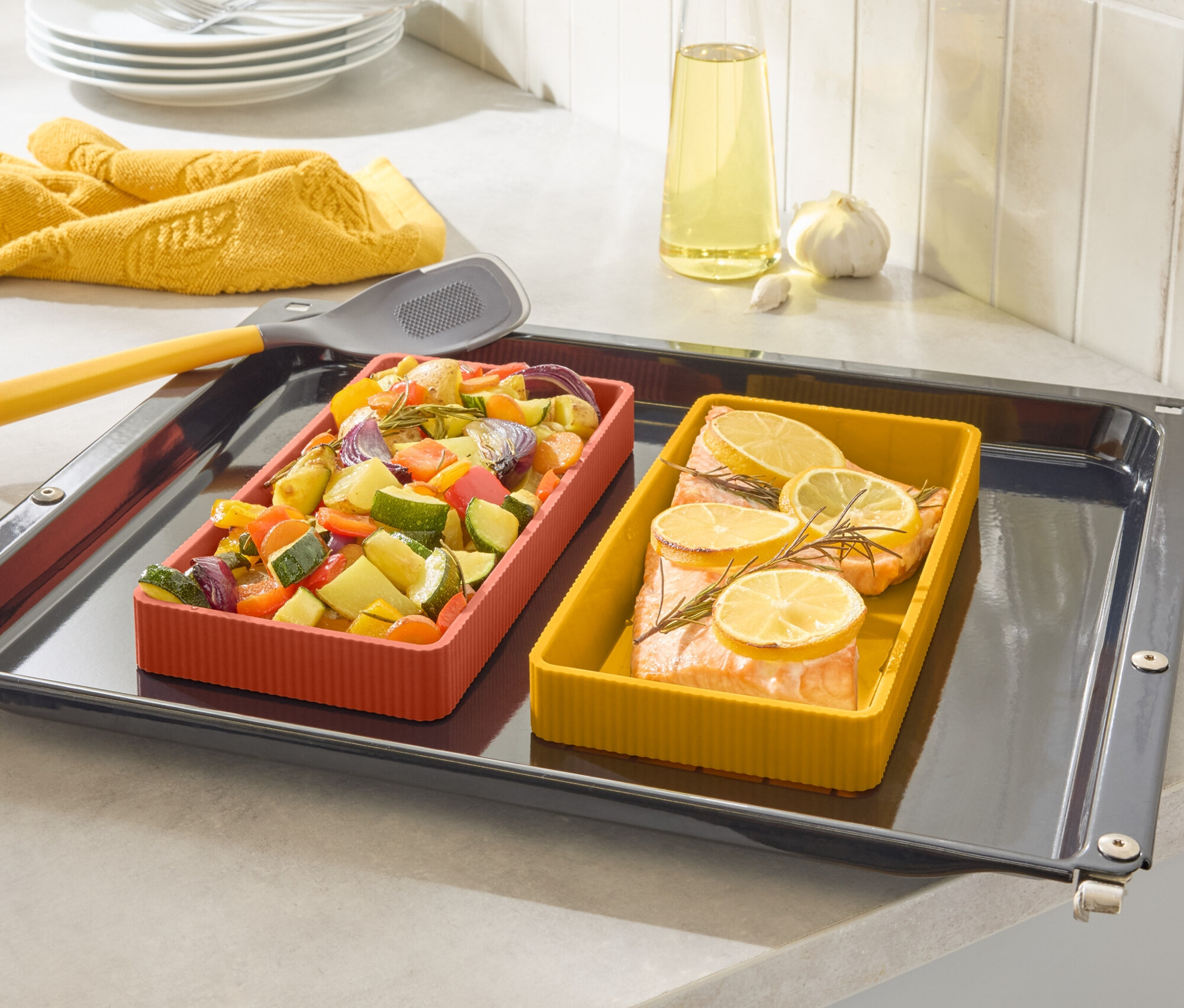 Auf einem Backblech befinden sich zwei farbige Auflaufformen, eine mit Lachs und Zitrone, die andere mit Gemüse.