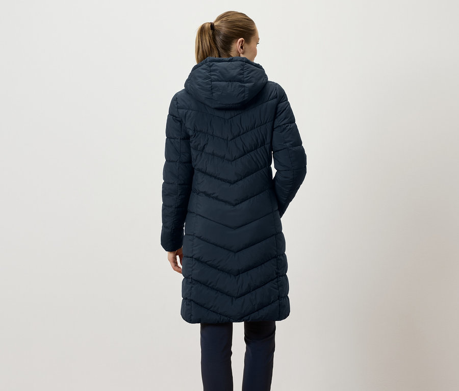 Rückansicht einer Frau mit braunen, zu einem Pferdeschwanz zusammengebundenen Haaren, die eine lange, gesteppte, marineblaue Jacke mit Kapuze trägt.