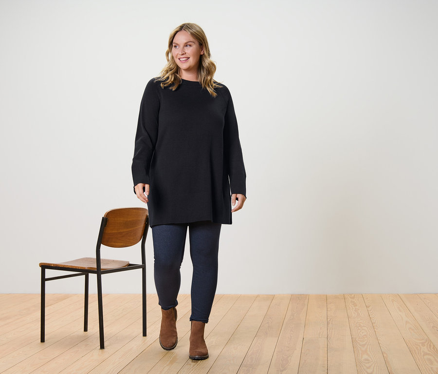 Eine Frau trägt einen langen, dunkelbraunen Strickpullover und gefütterte Leggings in Jeansoptik und geht.