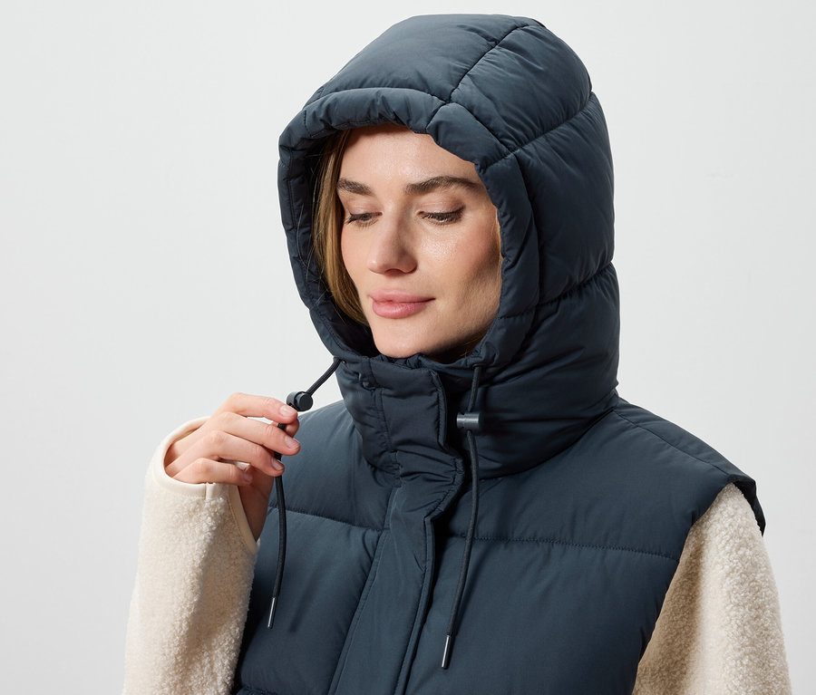 Frau justiert die Kapuze einer dunkelblauen Steppweste.