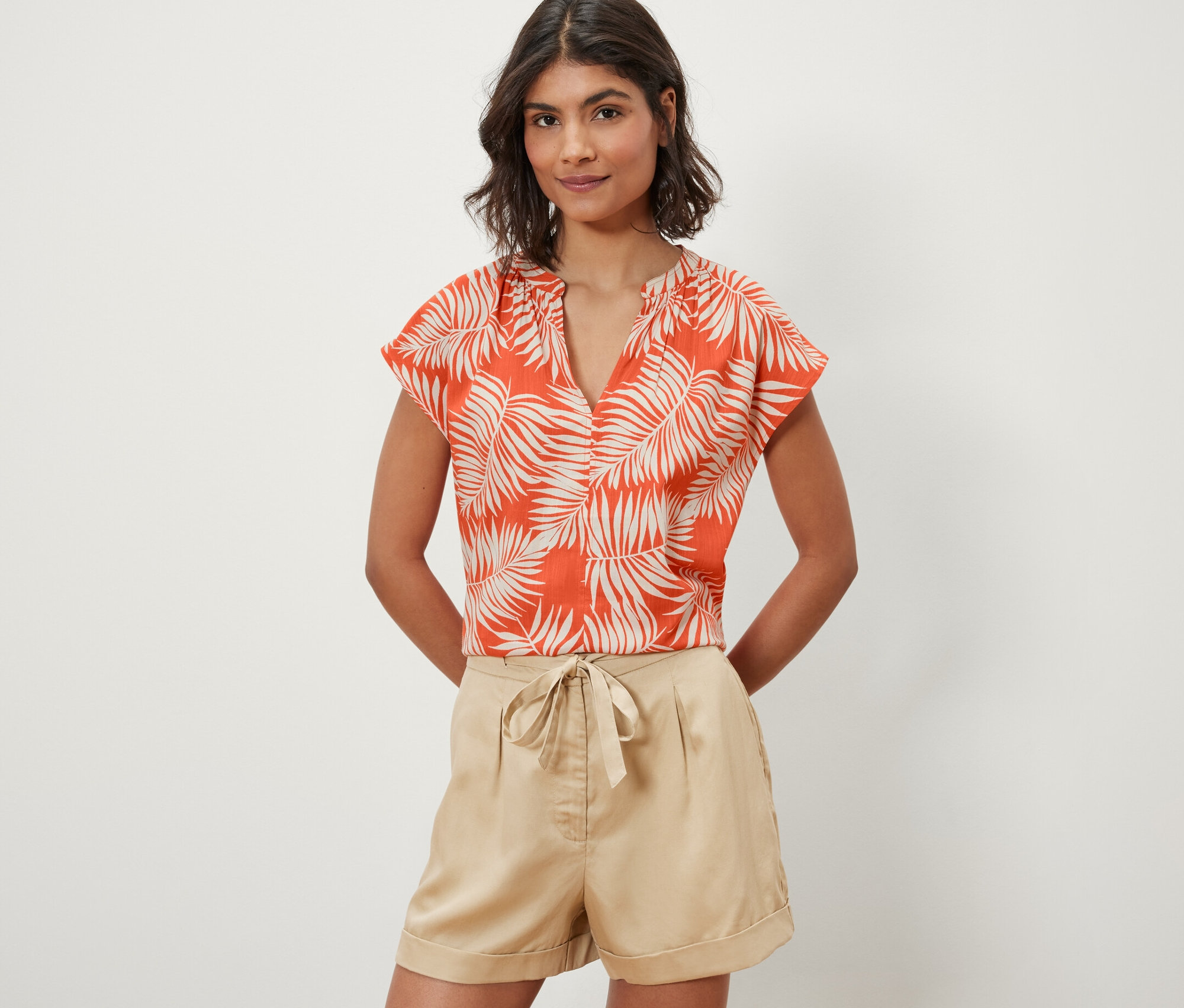 Frau trägt eine bedruckte Kurzarmbluse, orange.