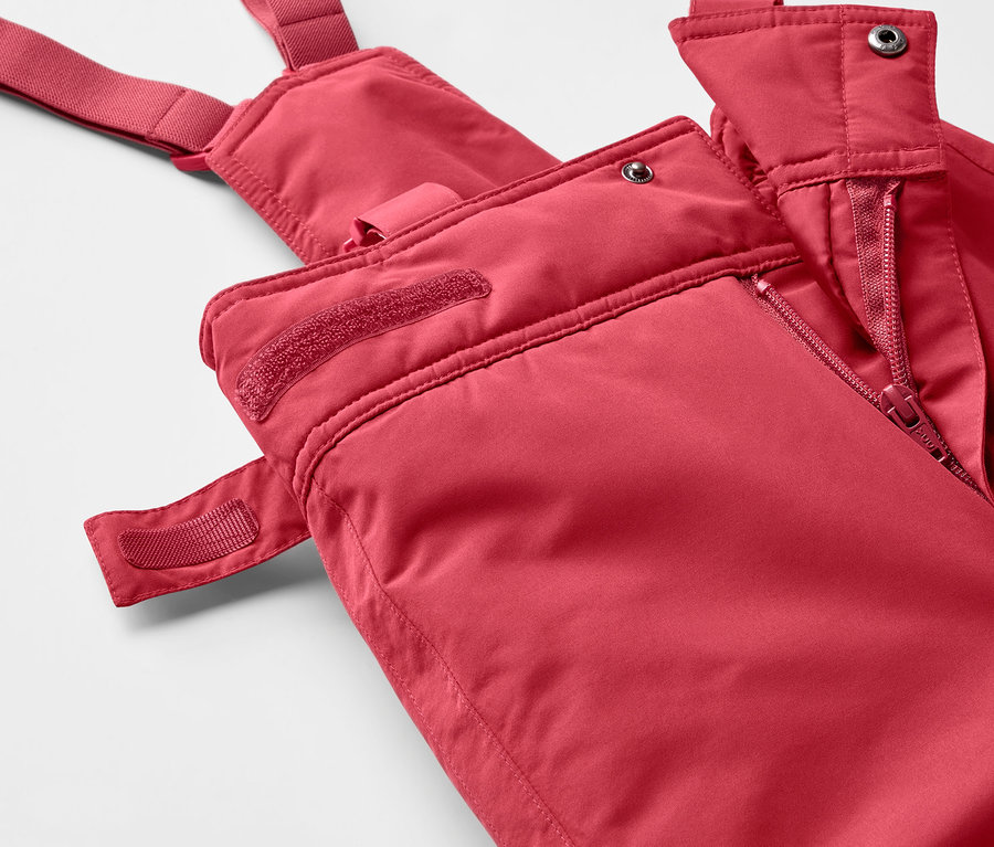 Detailaufnahme einer roten Skihose mit Latz und Reißverschluss.