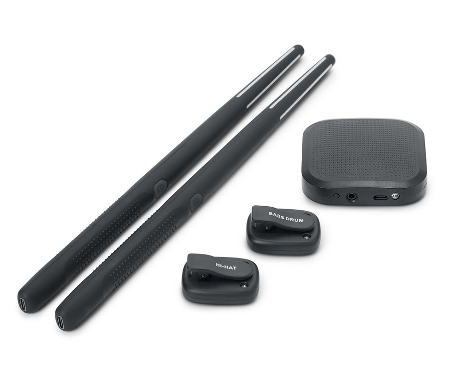 Zwei schwarze Drumsticks liegen nebeneinander. Eine schwarze Soundbox und zwei kleine schwarze Drum-Pads, eines mit der Aufschrift BASS DRUM und eines mit der Aufschrift HI-HAT, sind ebenfalls vorhanden.