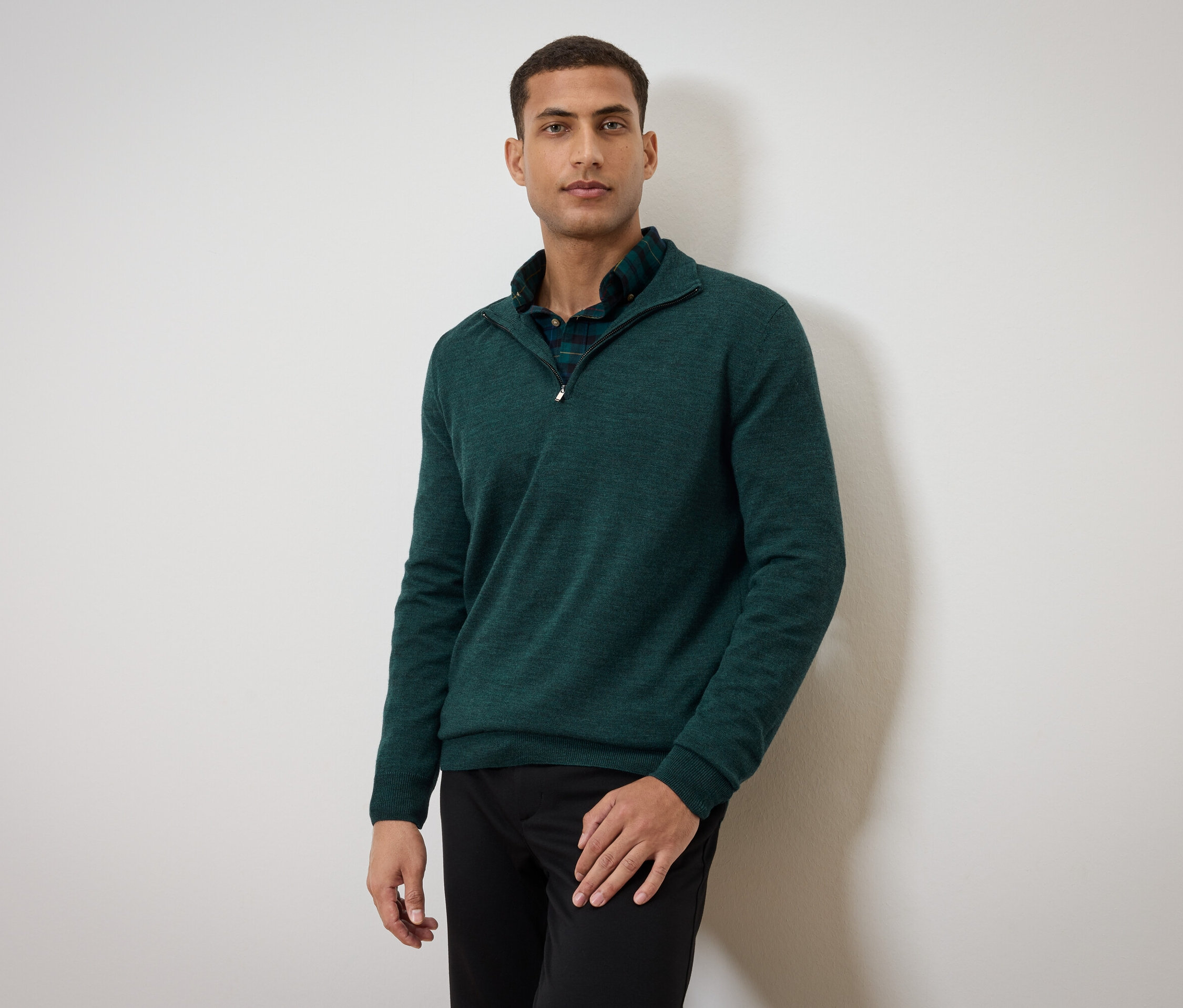 Mann posiert in grünem Pullover und schwarzen Hosen.