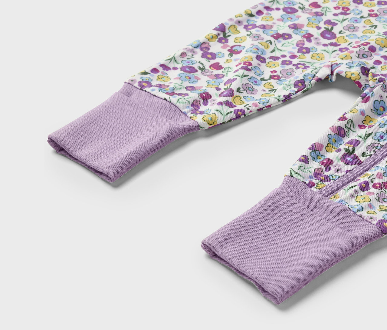 Detailaufnahme eines Baby-Overalls mit lila Bündchen und Blumenmuster.