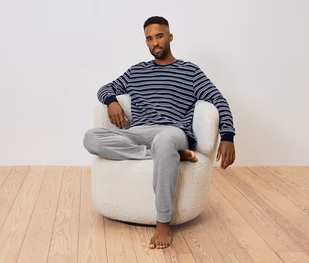 Mann sitzt in einem Sessel. Er trägt ein gestreiftes Langarmshirt und eine graue Jogginghose.