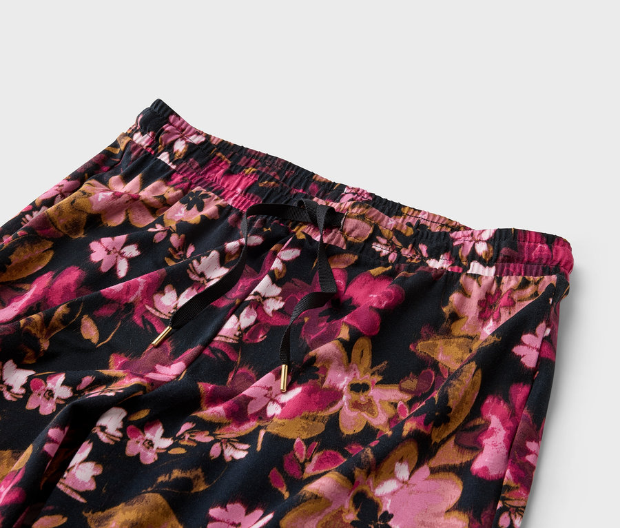 Nahaufnahme einer Hose mit Blumenmuster in Rosa- und Goldtönen, mit einem schwarzen Kordelzug.