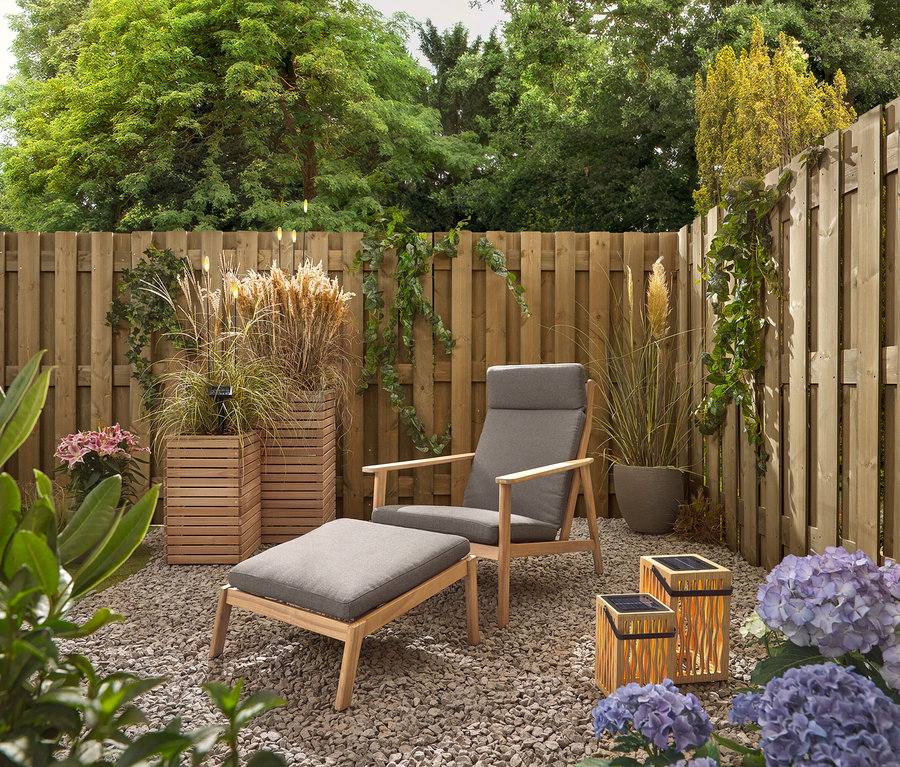 Ein Garten mit einem grauen Sessel und Hocker, zwei Bambus-Solar-Laternen und 5 LED-Solar-Spießen.