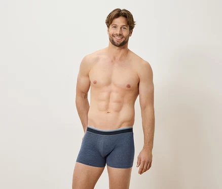 Mann mit freiem Oberkörper, der blaue Boxershorts trägt und lächelt.