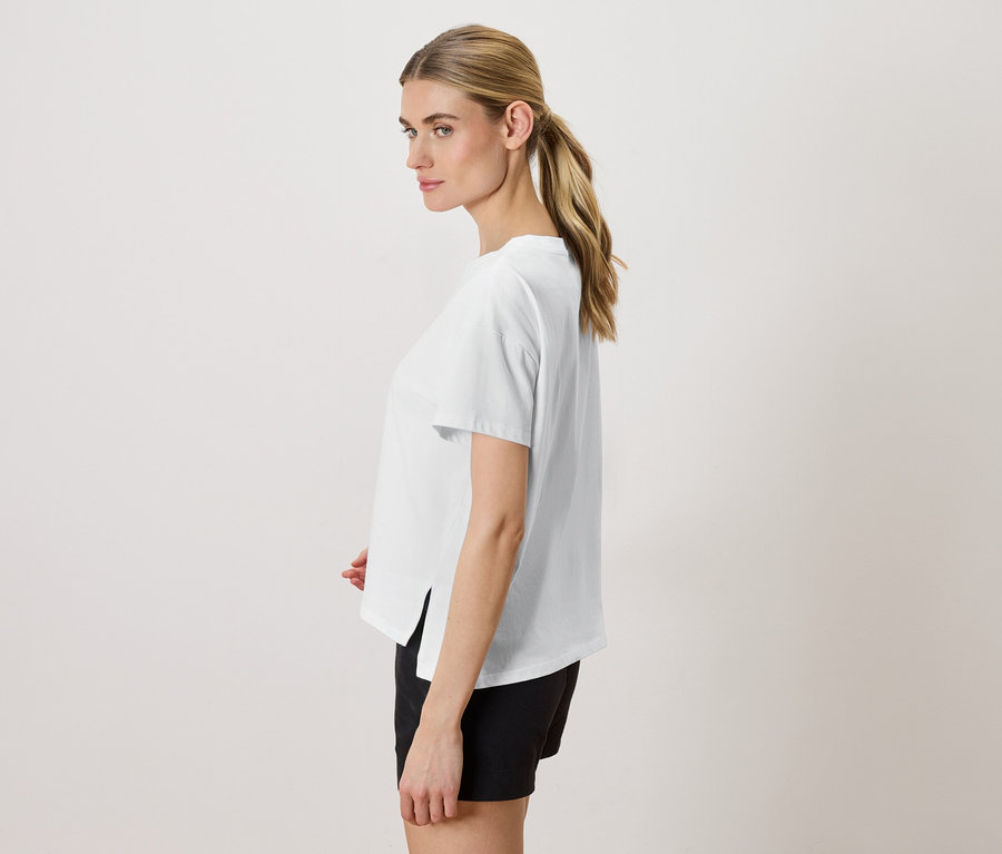 Frau mit blonden Haaren trägt ein weißes T-Shirt und schwarze Shorts, seitliche Ansicht.