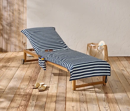Eine Liege mit blau-weiß gestreiftem Bezug steht auf einem Holzboden, daneben eine Tasche und Sandalen.