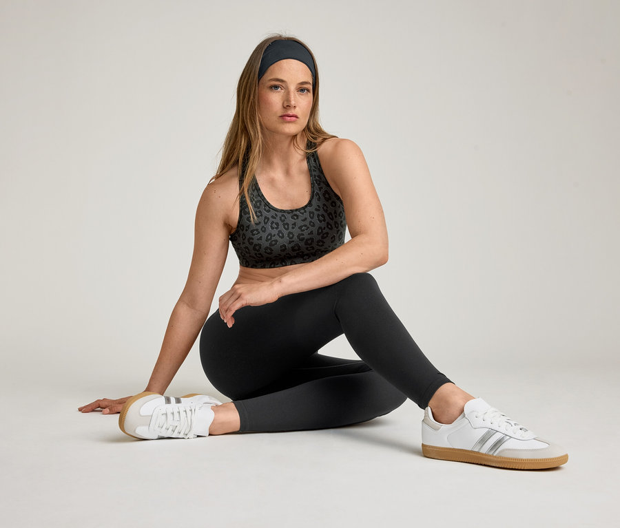 Frau sitzt mit Sport-BH, Stirnband und »ActiveSoft« Sportleggings. Sie trägt weiße Turnschuhe.