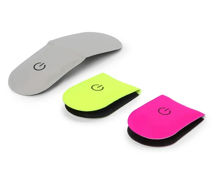 Drei Fersenpolster in Grau, Neon Gelb und Pink liegen auf einem weißen Hintergrund. Auf jedem Polster ist ein schwarzes Power-Symbol.