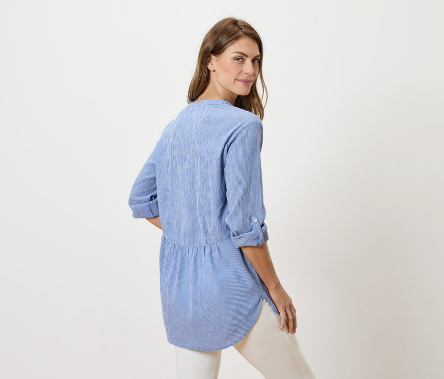 Frau blickt über ihre Schulter und trägt eine blaue Bluse und eine weiße Hose.