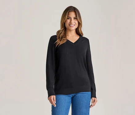 Lächelnde Frau mit langen braunen Haaren, die einen schwarzen V-Ausschnitt-Pullover und blaue Jeans trägt.