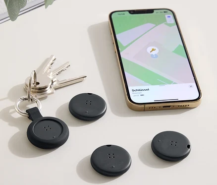 Auf einem Tisch liegen Schlüssel, ein Telefon mit einer Karten-App und drei schwarze Ortungsgeräte.