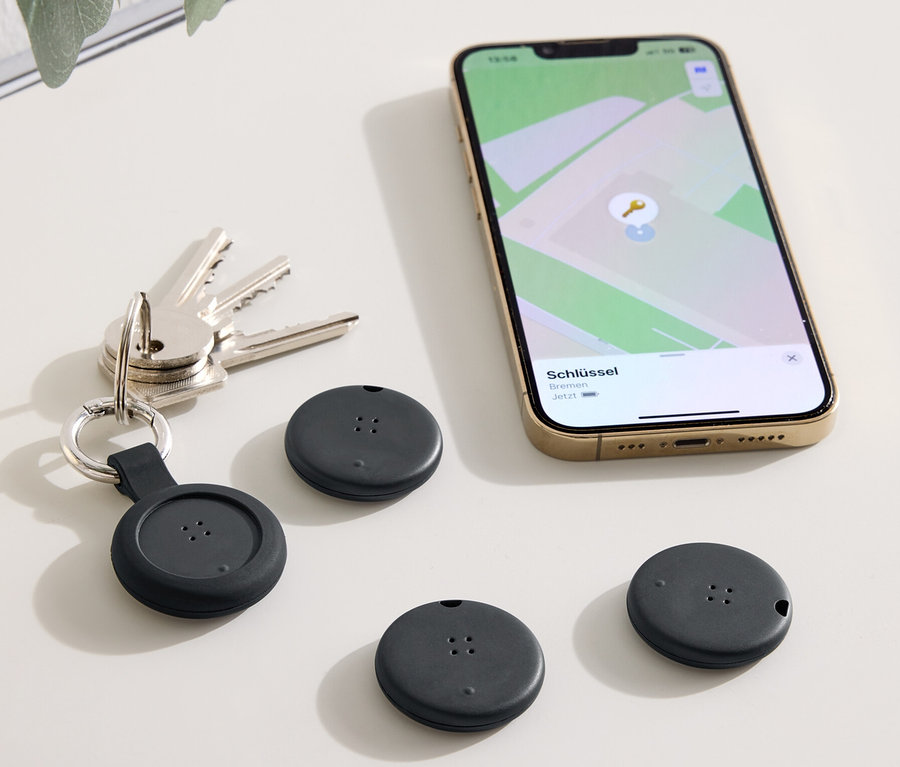 Auf einem Tisch liegen Schlüssel, ein Telefon mit einer Karten-App und drei schwarze Ortungsgeräte.