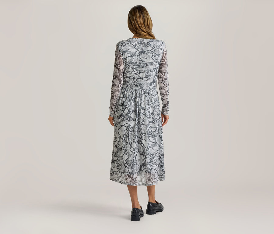 Frau von hinten in einem langärmeligen Midikleid mit Schlangenmuster und schwarzen Loafern.
