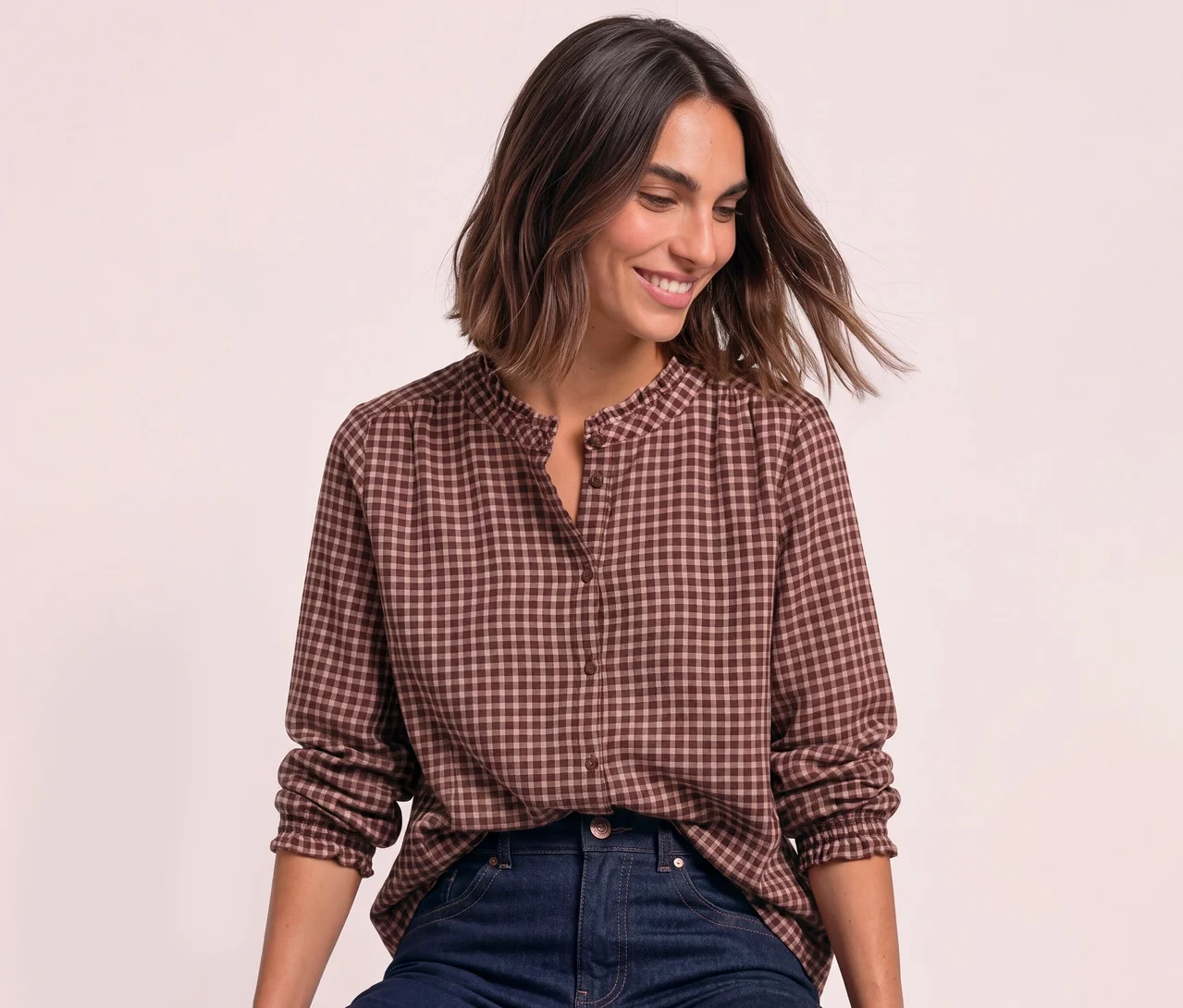 Lächelnde Frau in einer braun-hellrosa karierten Street One Bluse mit Rüschenkragen und dunkler Jeans.