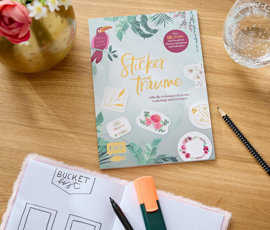 Das Buch "Stickerträume" liegt auf einem Tisch neben einem Tagebuch mit der Aufschrift "Bucket List", einem Textmarker und einem Bleistift.