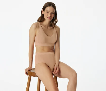 Frau sitzt auf einem Hocker und trägt einen SCHIESSER Soft BH mit Pads in Maple.