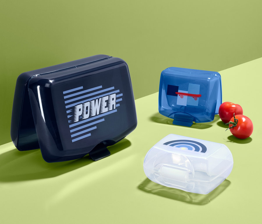 Drei Brotdosen in verschiedenen Farben auf grünem Hintergrund.