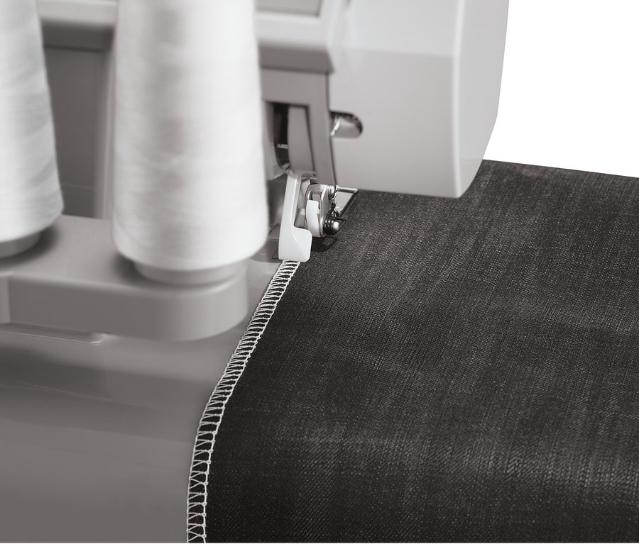 Detailaufnahme einer SINGER® Overlock-Nähmaschine »Heavy Duty 14HD854« beim Nähen von schwarzem Stoff mit weißem Faden.