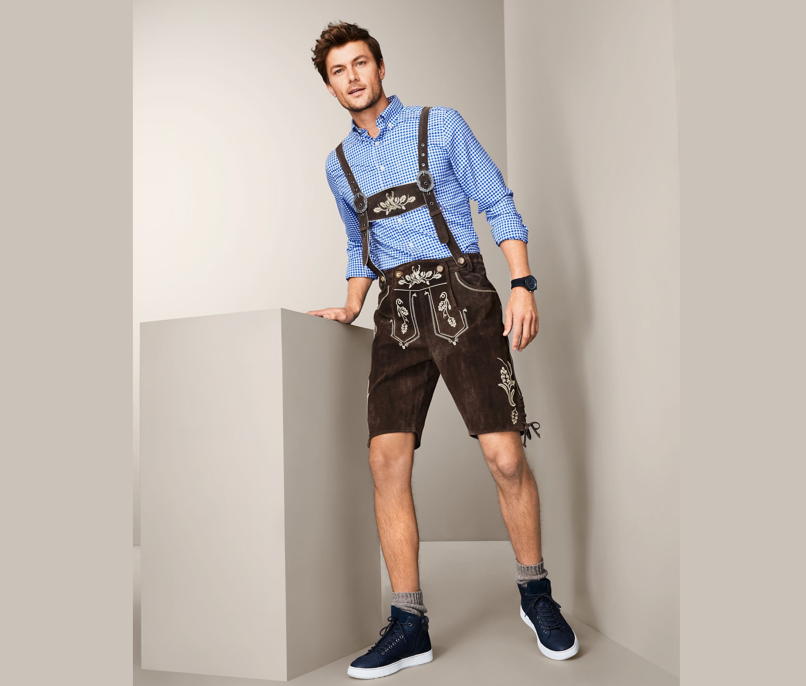 Mann posiert in blauem Hemd und Trachten-Lederhose.