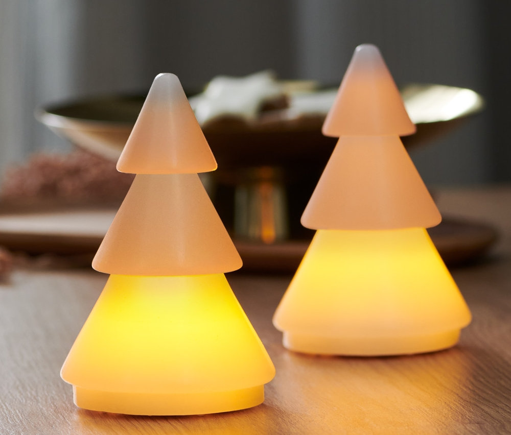 Zwei LED-Echtwachstannen stehen auf einem Holztisch. Im Hintergrund ist ein Fenster.