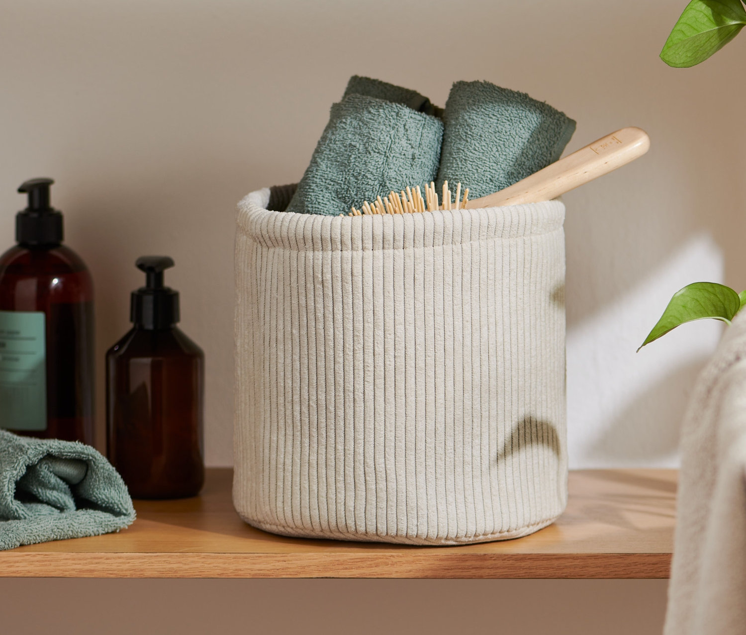 Auf einem Regal steht ein Aufbewahrungskorb, ca. 20 x 20 x 20 cm, in dem gefaltete Handtücher und eine Bürste liegen.