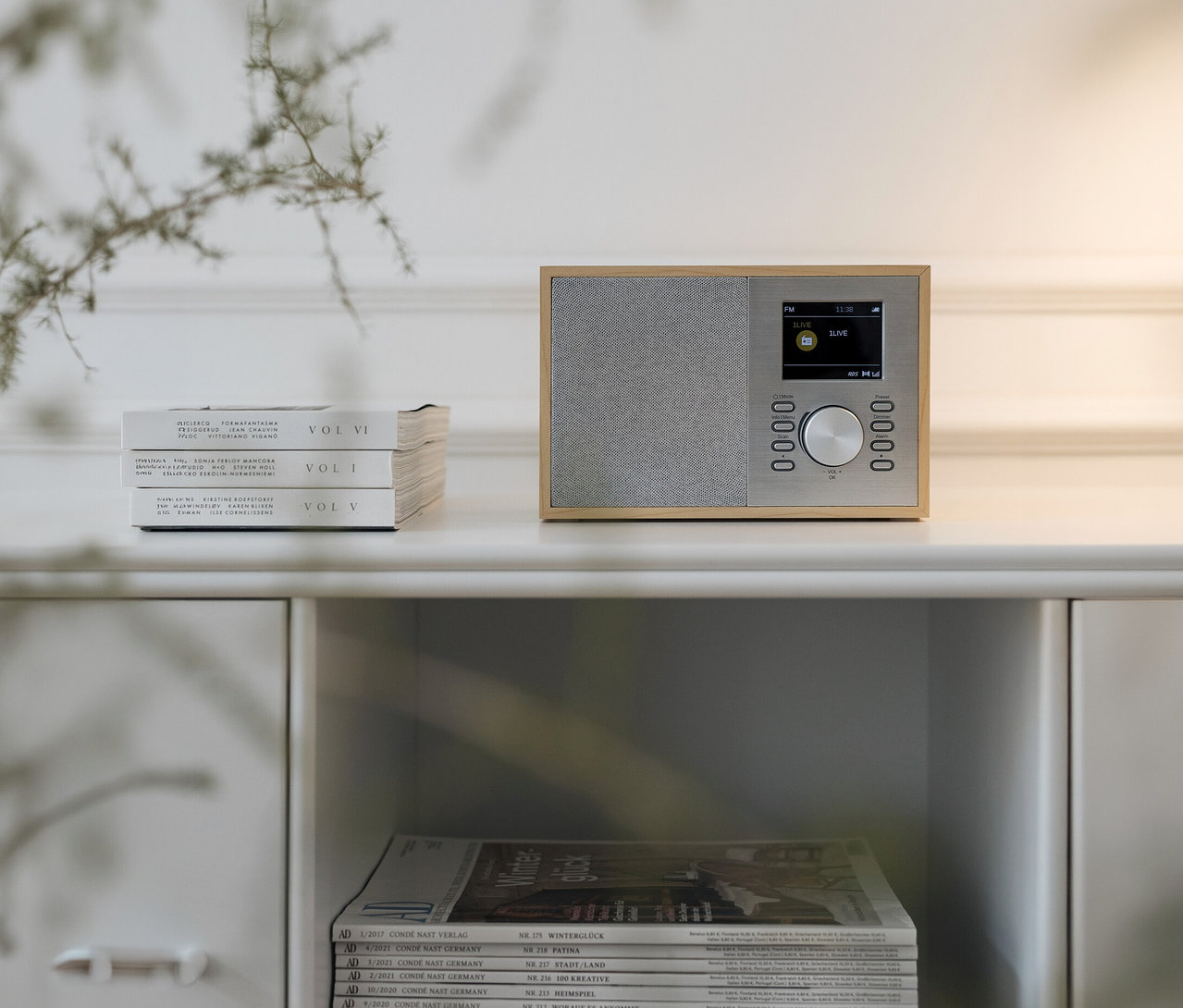 DAB+/FM-Digitalradio mit Bluetooth® steht auf einem weißen Schrank neben drei Büchern. Darunter liegen Zeitschriften.