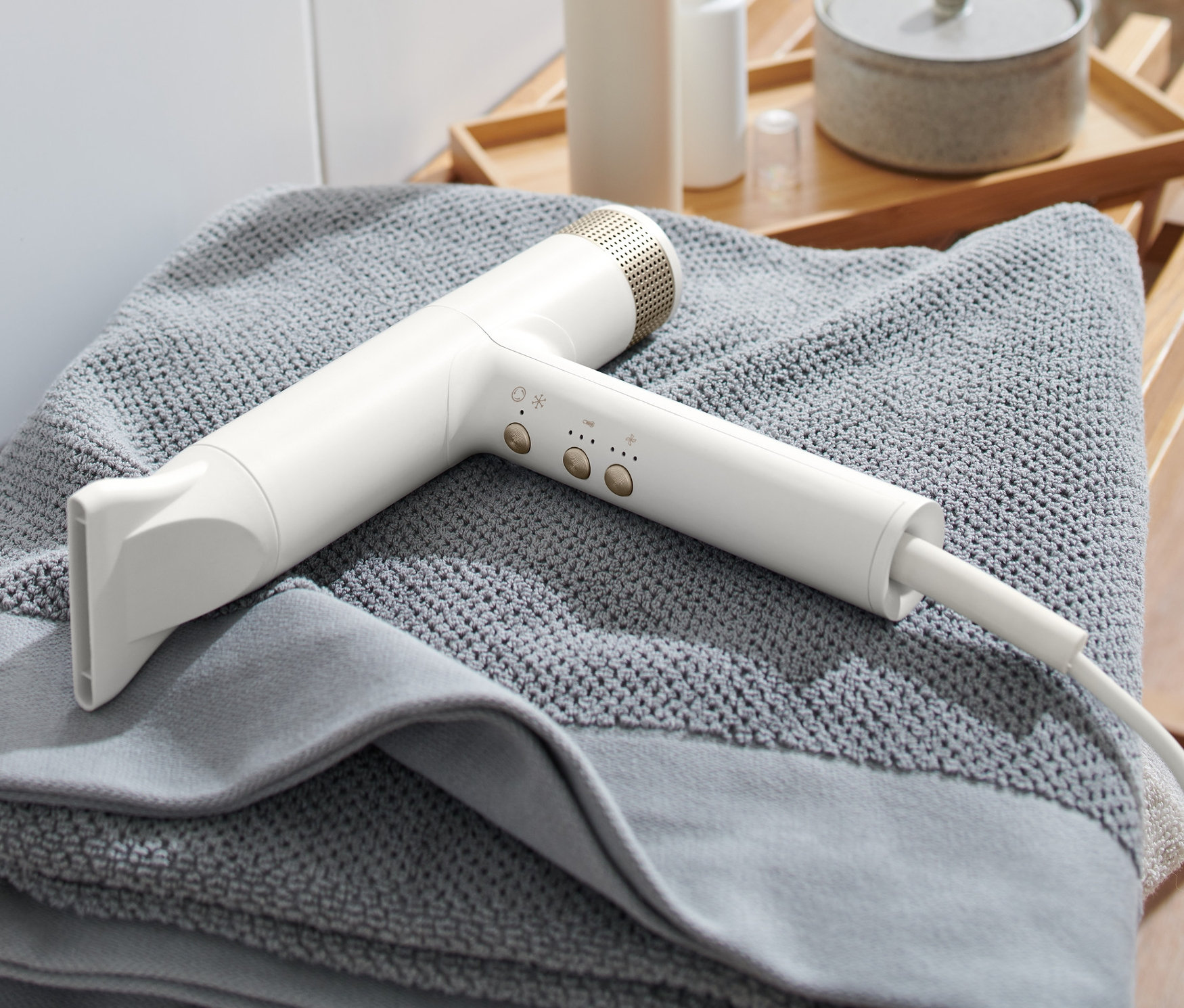 Ein weißer Premium-Haartrockner liegt auf einem grauen Handtuch auf einem Holzhocker.