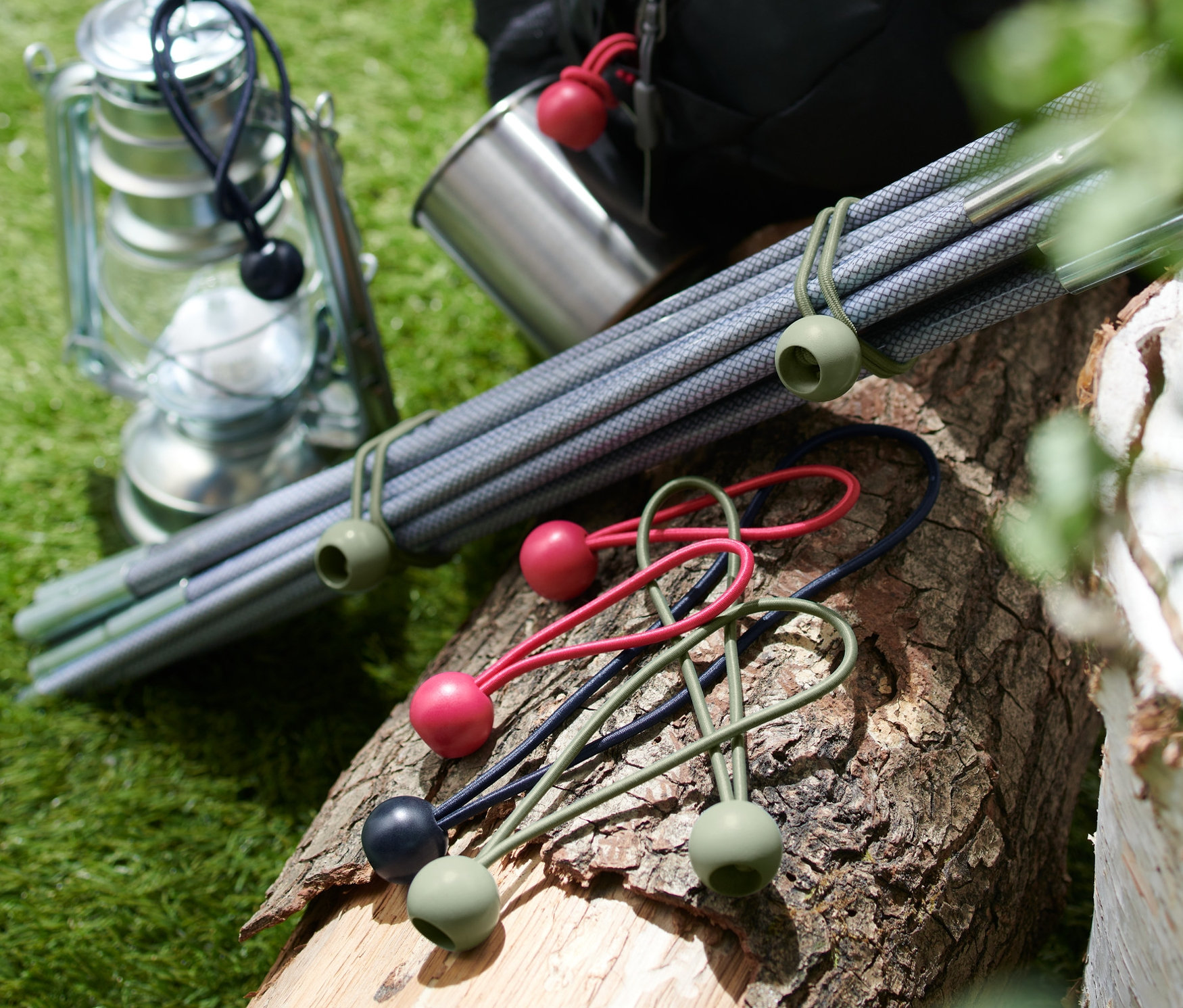 Auf einem Holzblock liegen 12 Spanngummis mit Kugel, daneben eine Laterne, ein Metallbecher, Stangen und ein Rucksack.