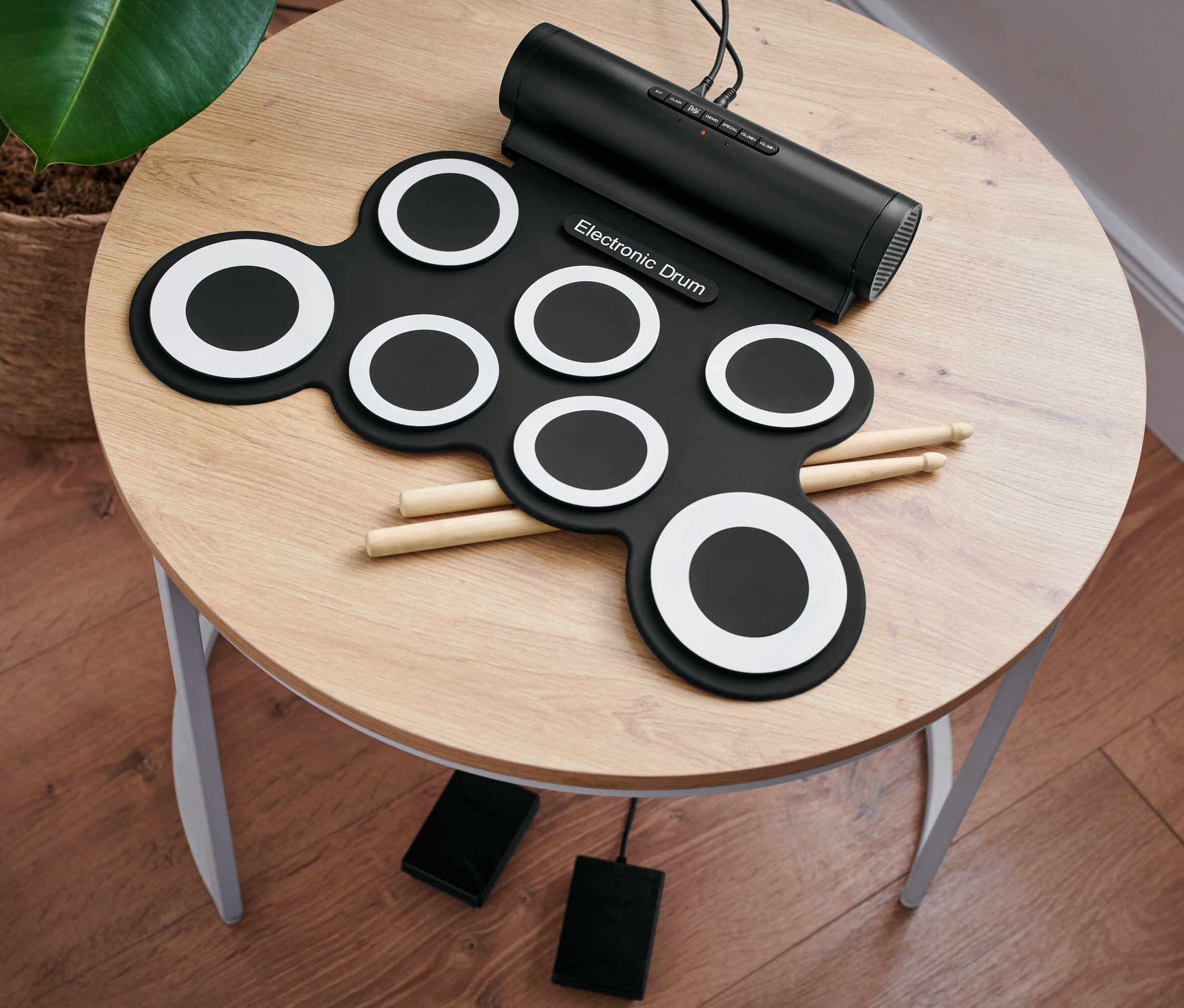 Auf einem runden Tisch liegt ein elektronisches Schlagzeug-Set mit Drumsticks und Pedalen.