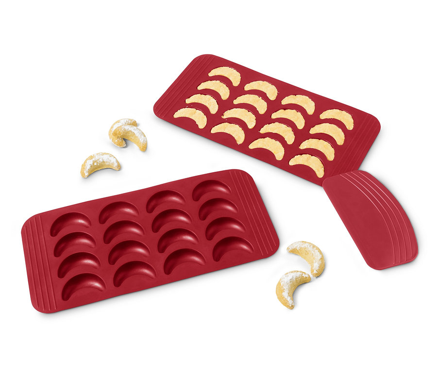 Zwei rote Vanillekipferl-Backmatten, eine mit gebackenen Kipferln gefüllt, und ein paar Kipferl neben den Matten.