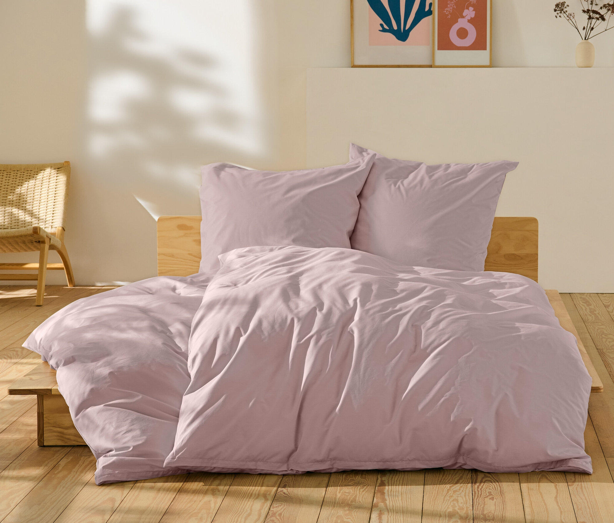 Rosafarbene Perkal-Bettwäsche in Normal- und Übergröße auf einem Bett.