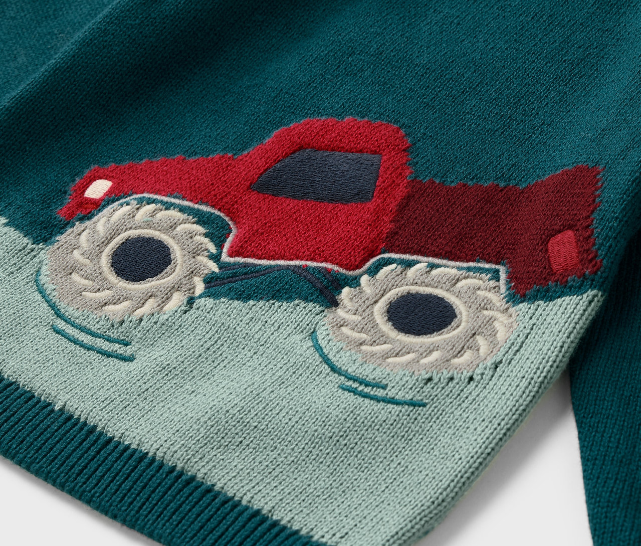 Detailansicht eines Kinder-Strickpullovers mit rotem Lastwagen-Motiv.