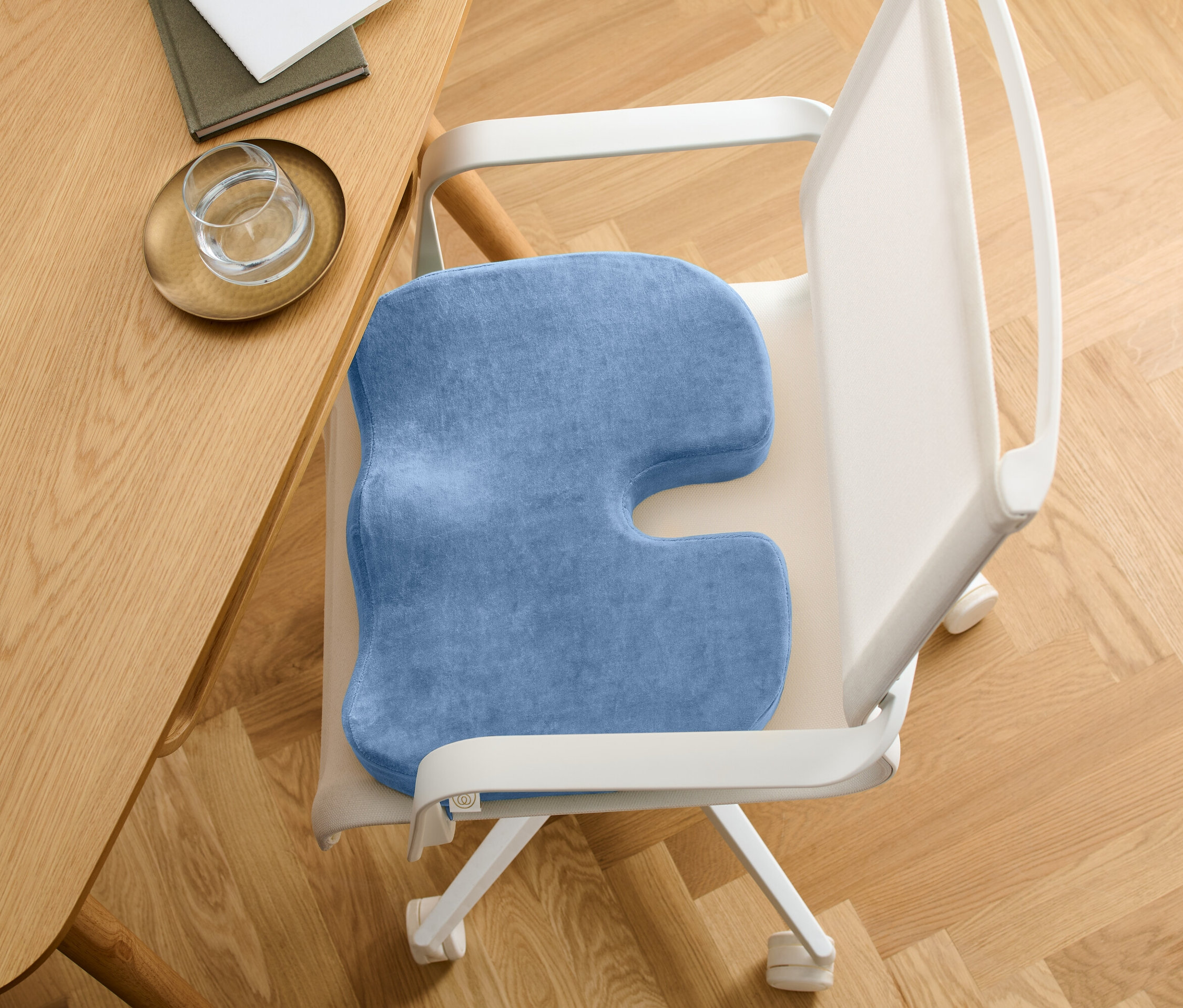 Detailaufnahme eines blauen orthopädischen Sitzkissens auf einem weißen Bürostuhl an einem Tisch.