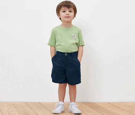 Ein Junge steht mit den Händen in den Taschen seiner Kinder-Funktionsshorts.