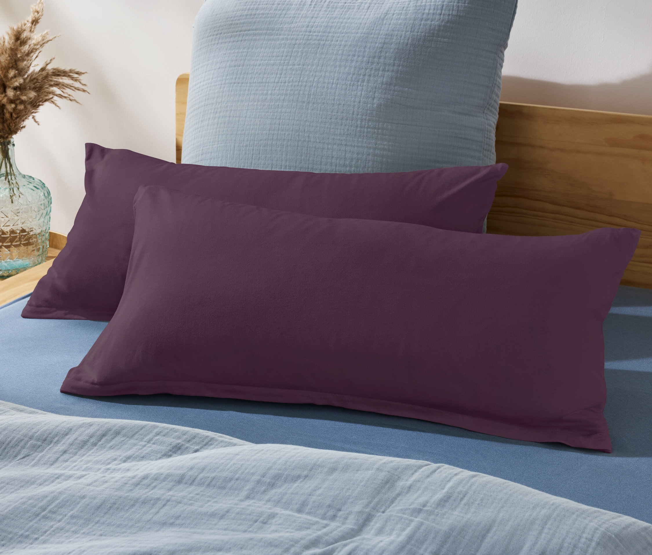 Zwei lilafarbene Kissen auf einem Bett mit blauem Bettlaken und einem blauen Kissen im Hintergrund.